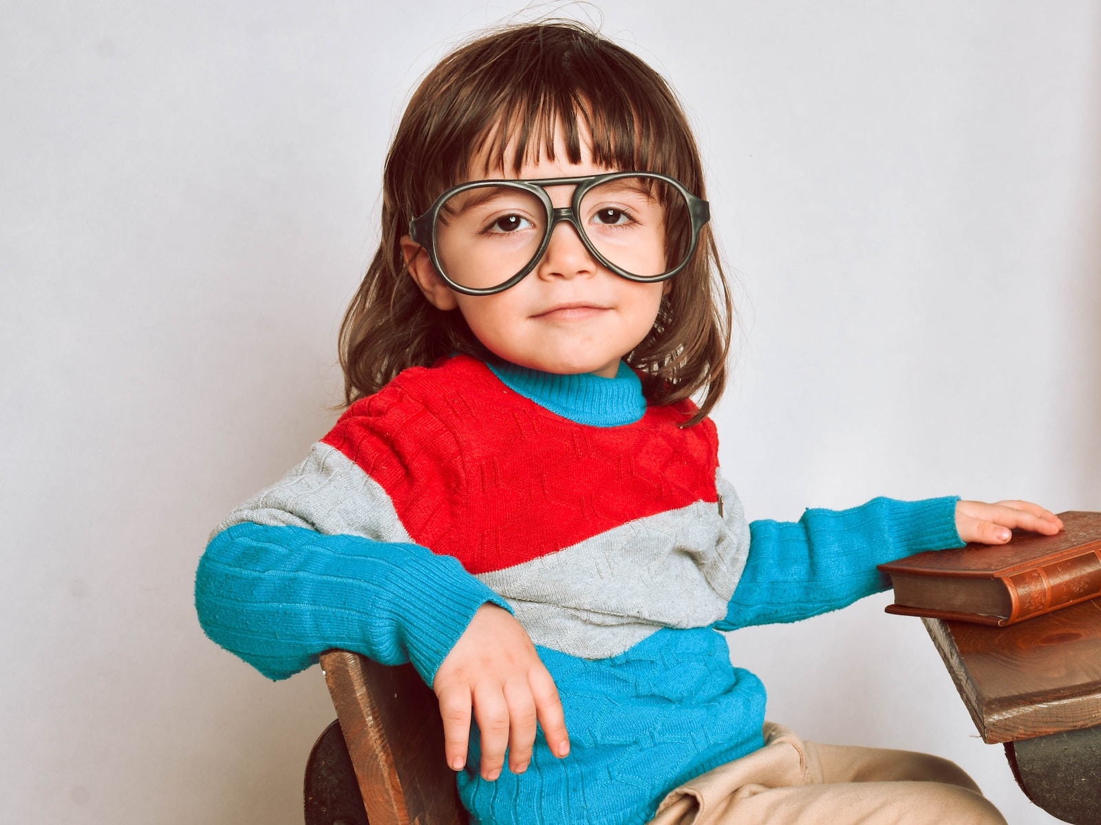girl in red framed eyeglasses and gray sweater sitting on brown wooden chair