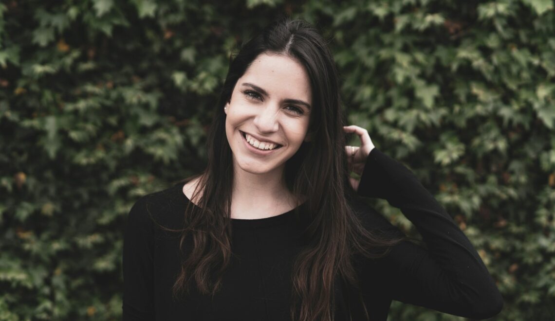 a smiling woman in a black top stands in front of a bush